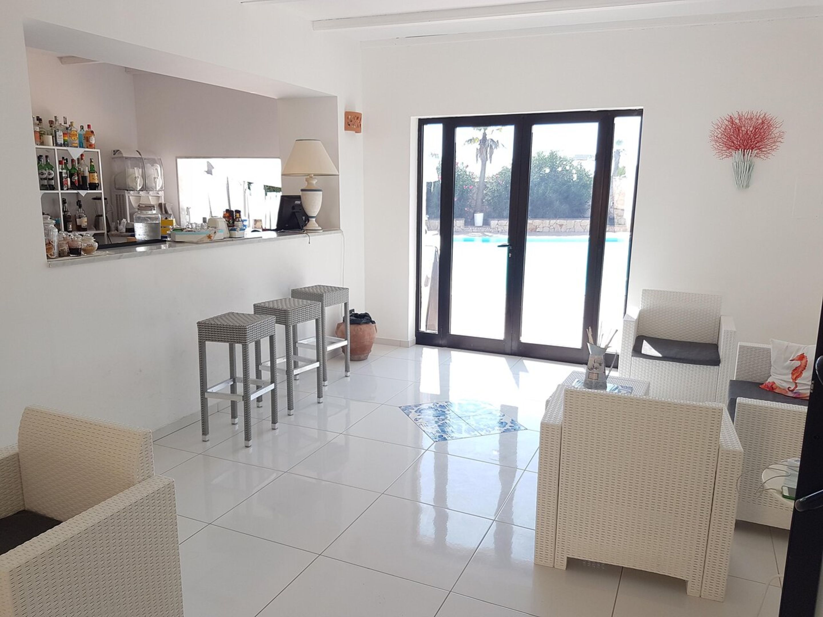 A spacious living area with a kitchen counter, bar stools, and a large sliding glass door leading to a pool.