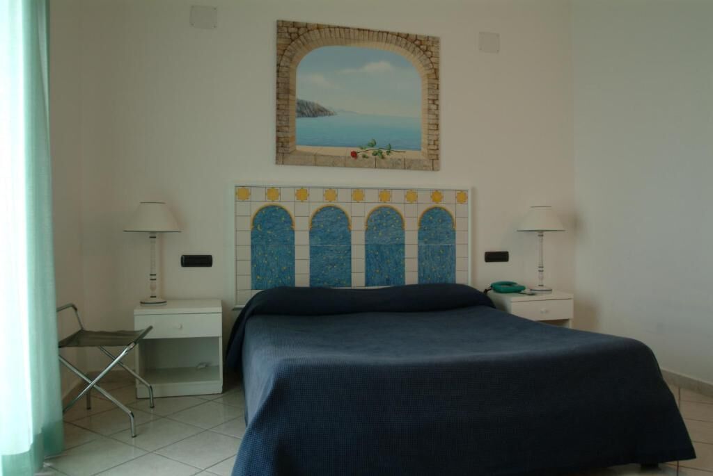 A bedroom with a bed, two bedside tables, a chair, and a wall-mounted painting.