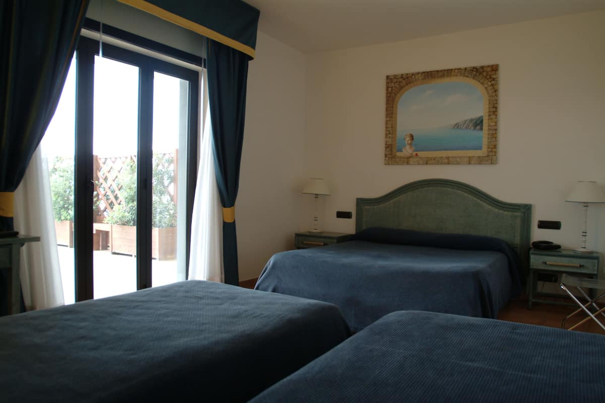 Une chambre d’hôtel avec deux lits, un tableau au mur et une vue sur l’extérieur par une grande fenêtre.