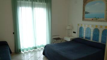 A hotel room with two beds, a window with curtains, a small table with a lamp, and a decorative wall tile.