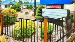 Schild für das Americas Best Value Inn by Sonesta, umgeben von einem eingezäunten Bereich mit Grünpflanzen und blauem Himmel.