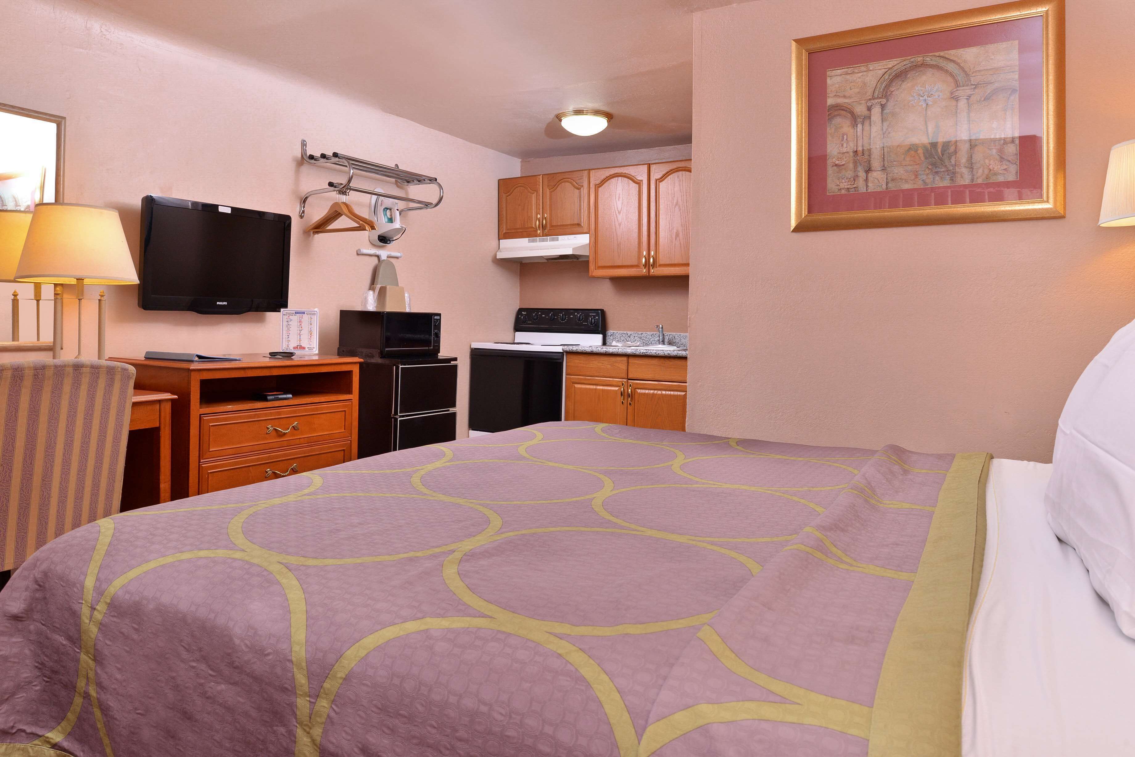 Quarto de hotel com uma cama, uma escrivaninha com televisão, micro-ondas, fogão e um quadro na parede.