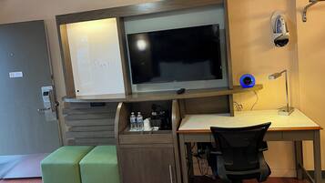 Een moderne hotelkamer met een grote flatscreen televisie, een bureau met stoel, een kleine groene bank en een minibar.
