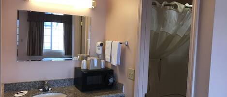A bathroom with a sink, a mirror, a hairdryer, and a shower curtain.