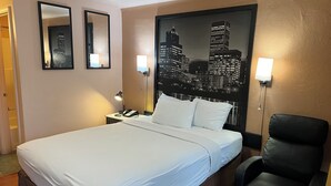 Ein Hotelzimmer mit einem großen Bett, zwei Nachttischlampen, einem schwarzen Ledersessel und einem Stadtbild an der Wand.