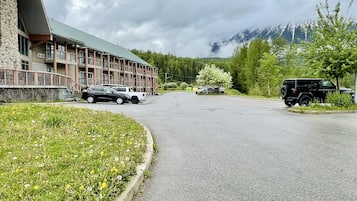 Un edificio de varios pisos, un estacionamiento con varios coches y un telón de fondo montañoso.