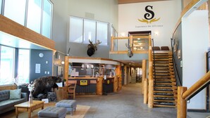 A spacious lobby with a wooden staircase, a reception desk, and a mounted deer head.