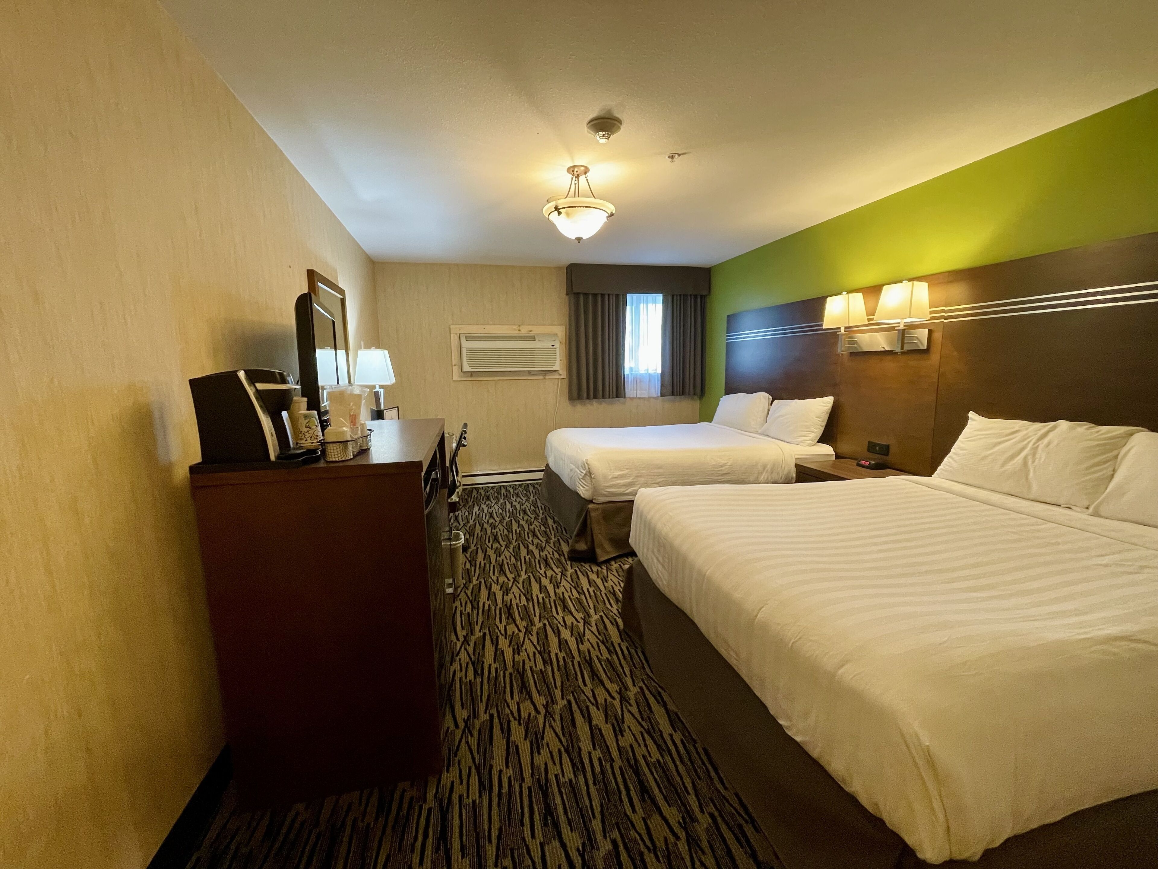 Een hotelkamer met twee bedden, een bureau, een spiegel, een lamp en een airconditioning.