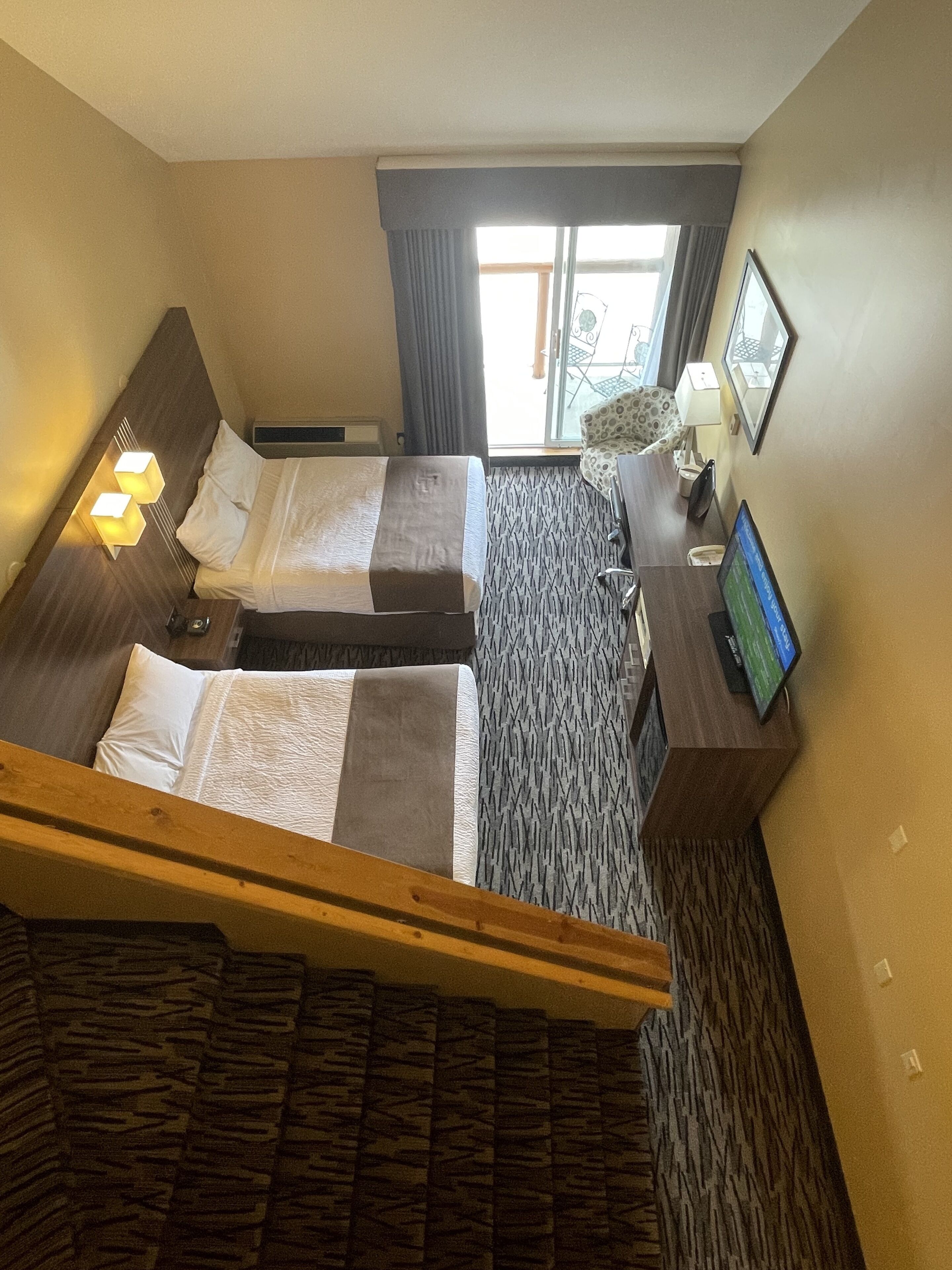 A hotel room with two beds, a desk, a TV, and a window with curtains.