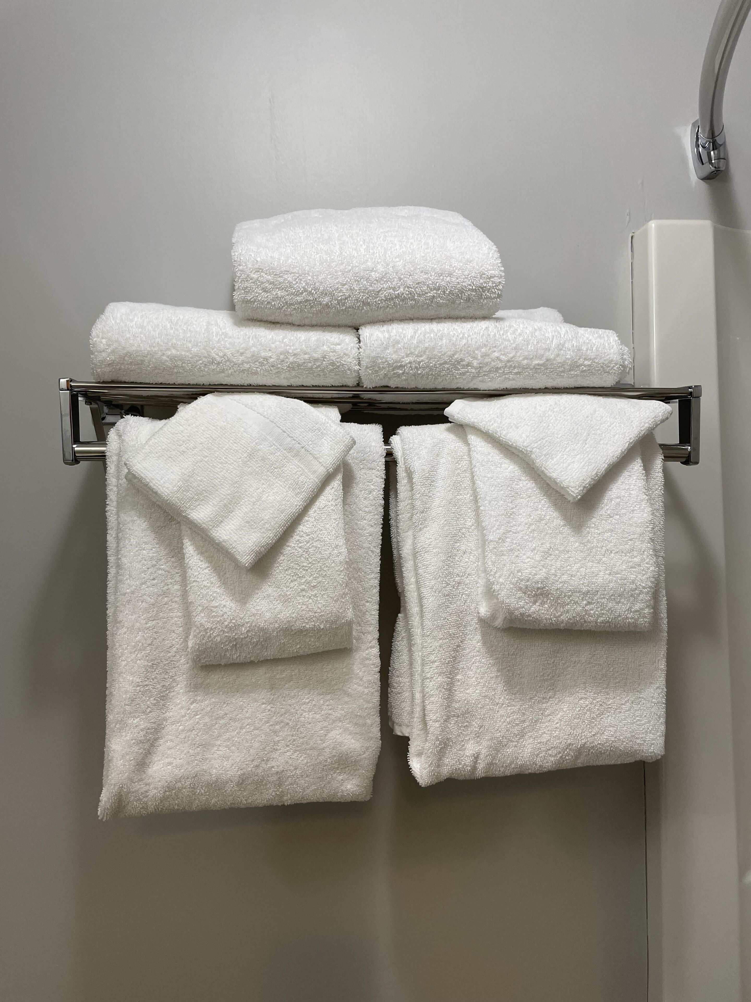 A set of white towels neatly folded and hung on a metal towel rack in a bathroom.