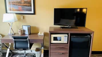 A hotel room with a wooden desk, a television, a microwave, and a framed picture on the wall.