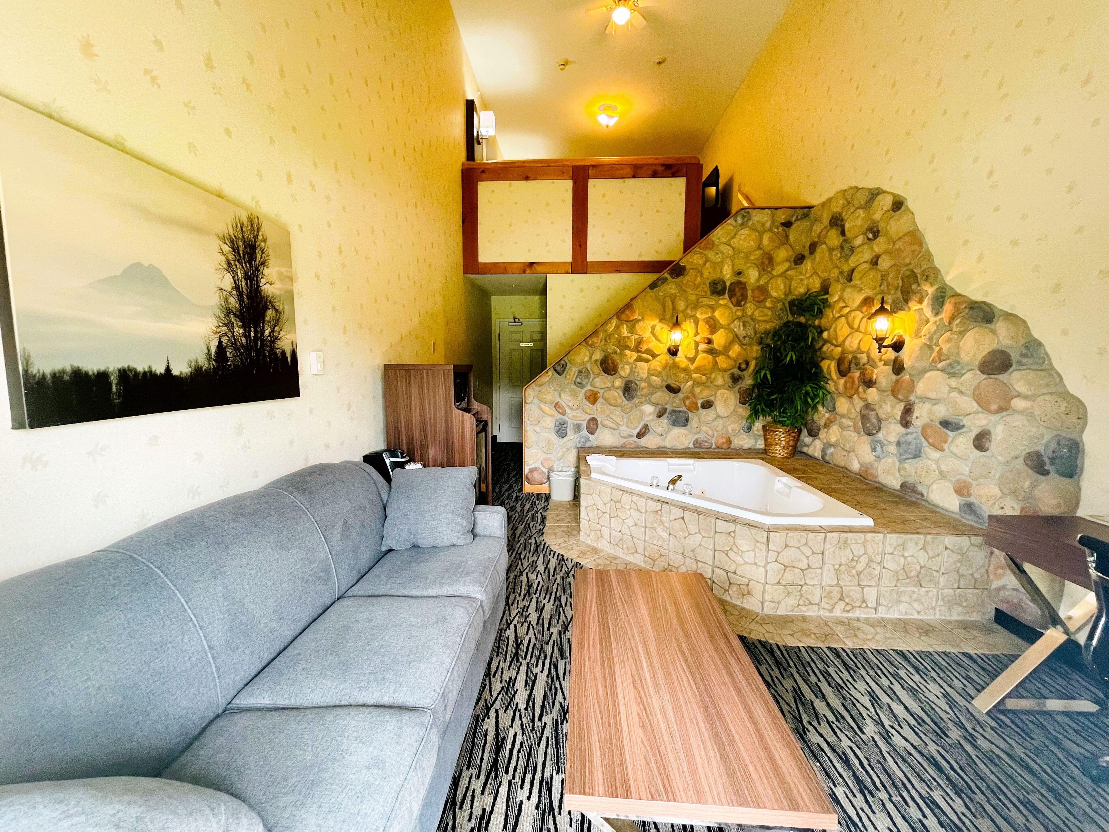 Un salon moderne avec un canapé gris, un mur en pierre, un escalier en bois et une baignoire en pierre.