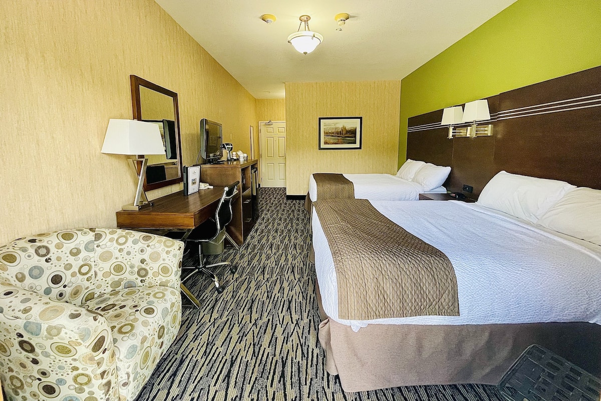 Quarto de hotel com duas camas, uma escrivaninha, uma cadeira e uma televisão.