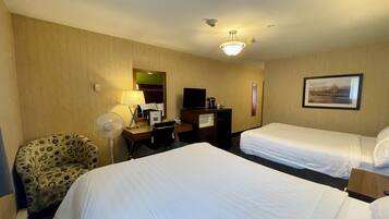 A hotel room with two beds, a desk with a computer, a chair, a fan, and a picture on the wall.
