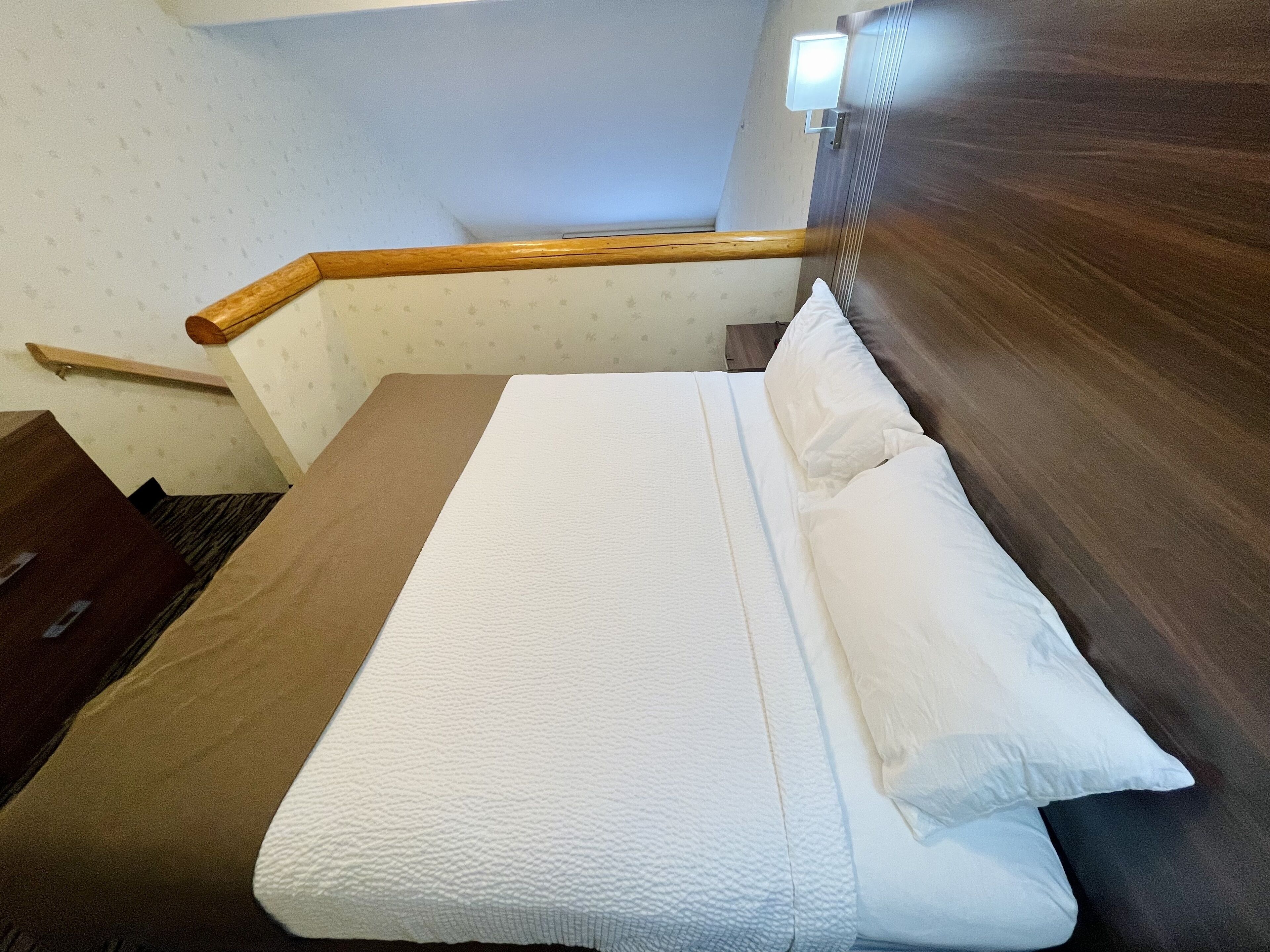 Un lit bien fait, avec du linge de lit blanc, une tête de lit en bois et une petite table de chevet.