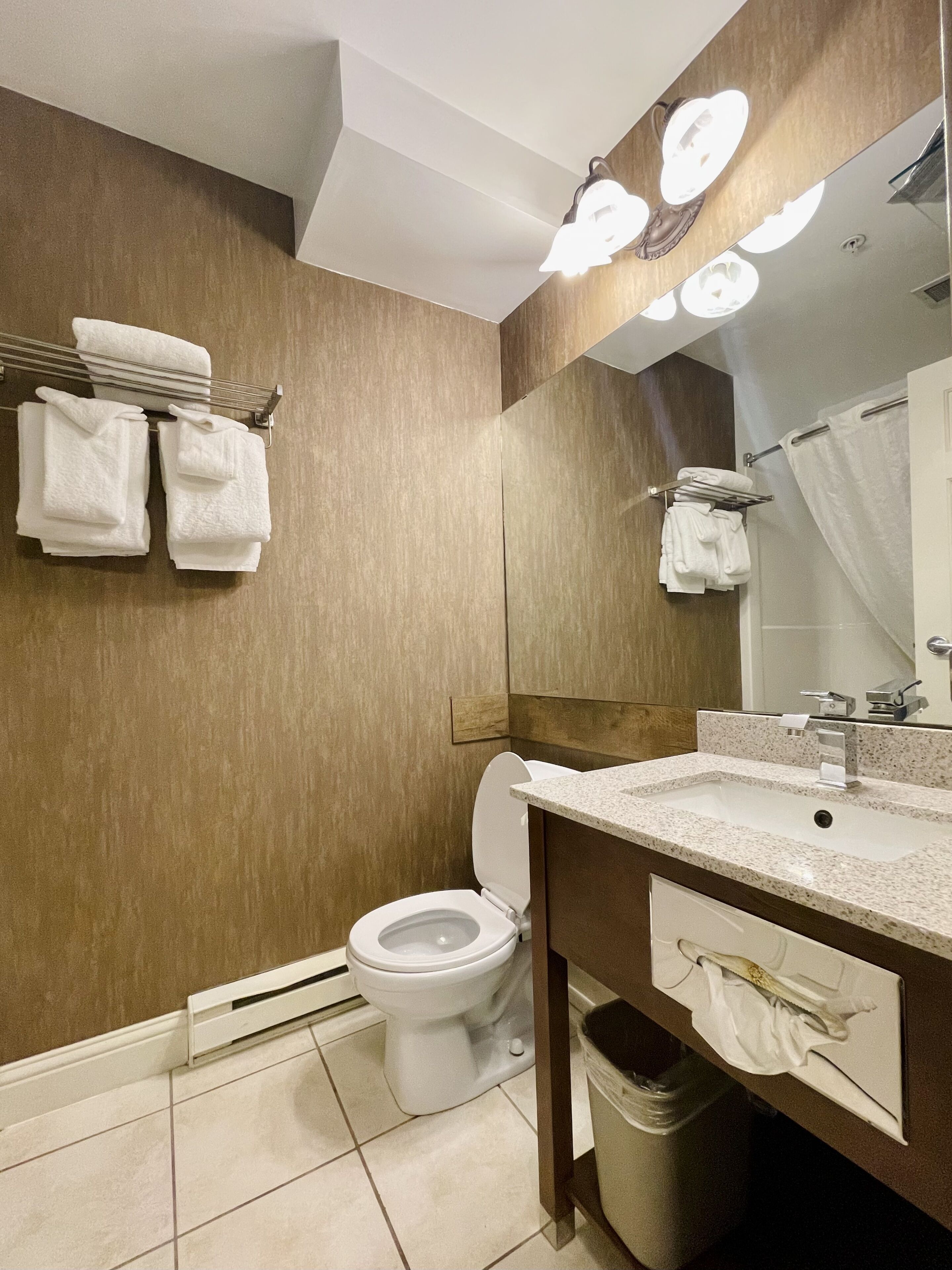 Een moderne badkamer met toilet, wastafel en spiegel. Handdoeken hangen aan een rek en er is een douchegordijn.