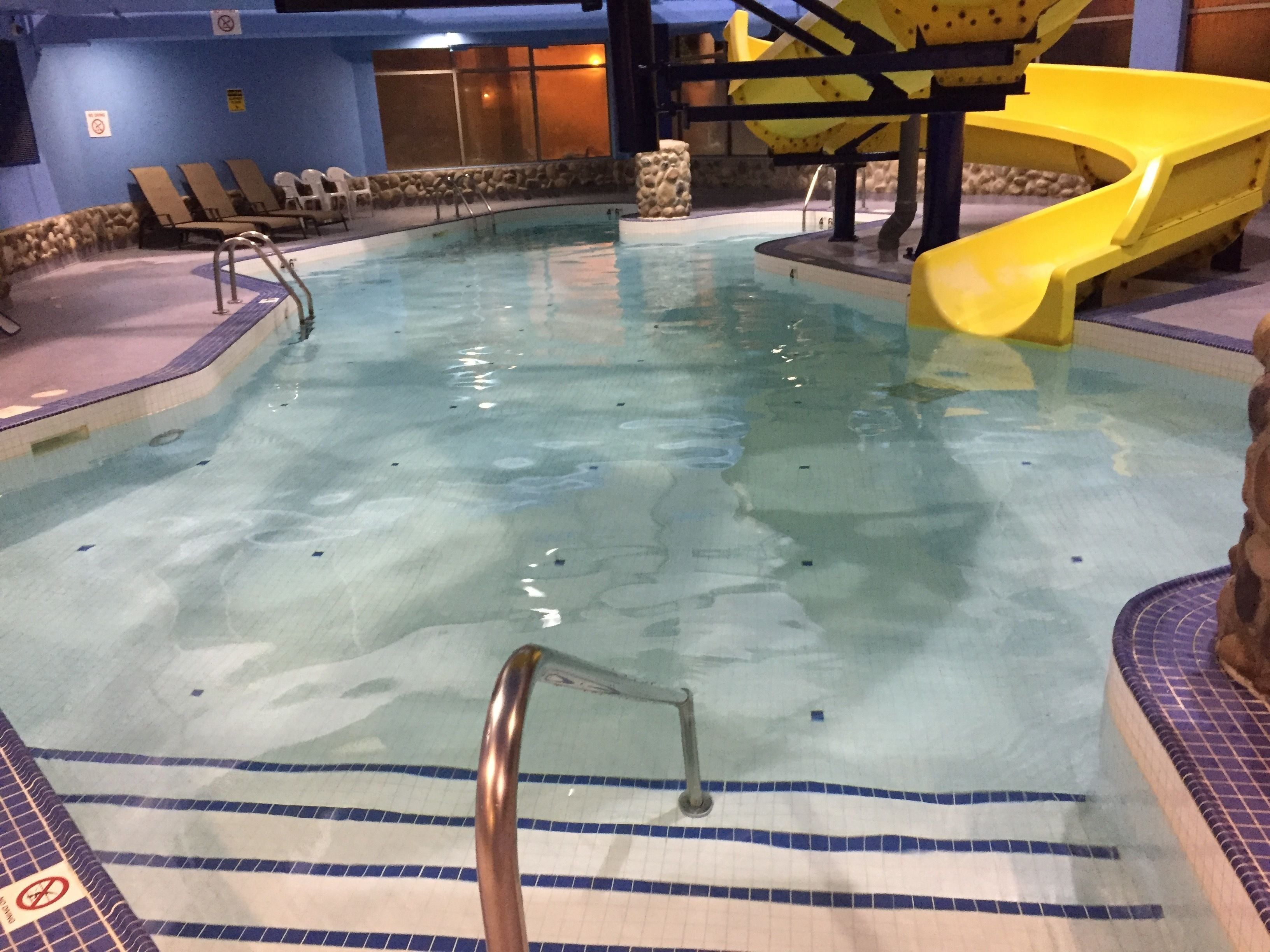 An indoor swimming pool with a yellow slide, lounge chairs, and a stone wall.