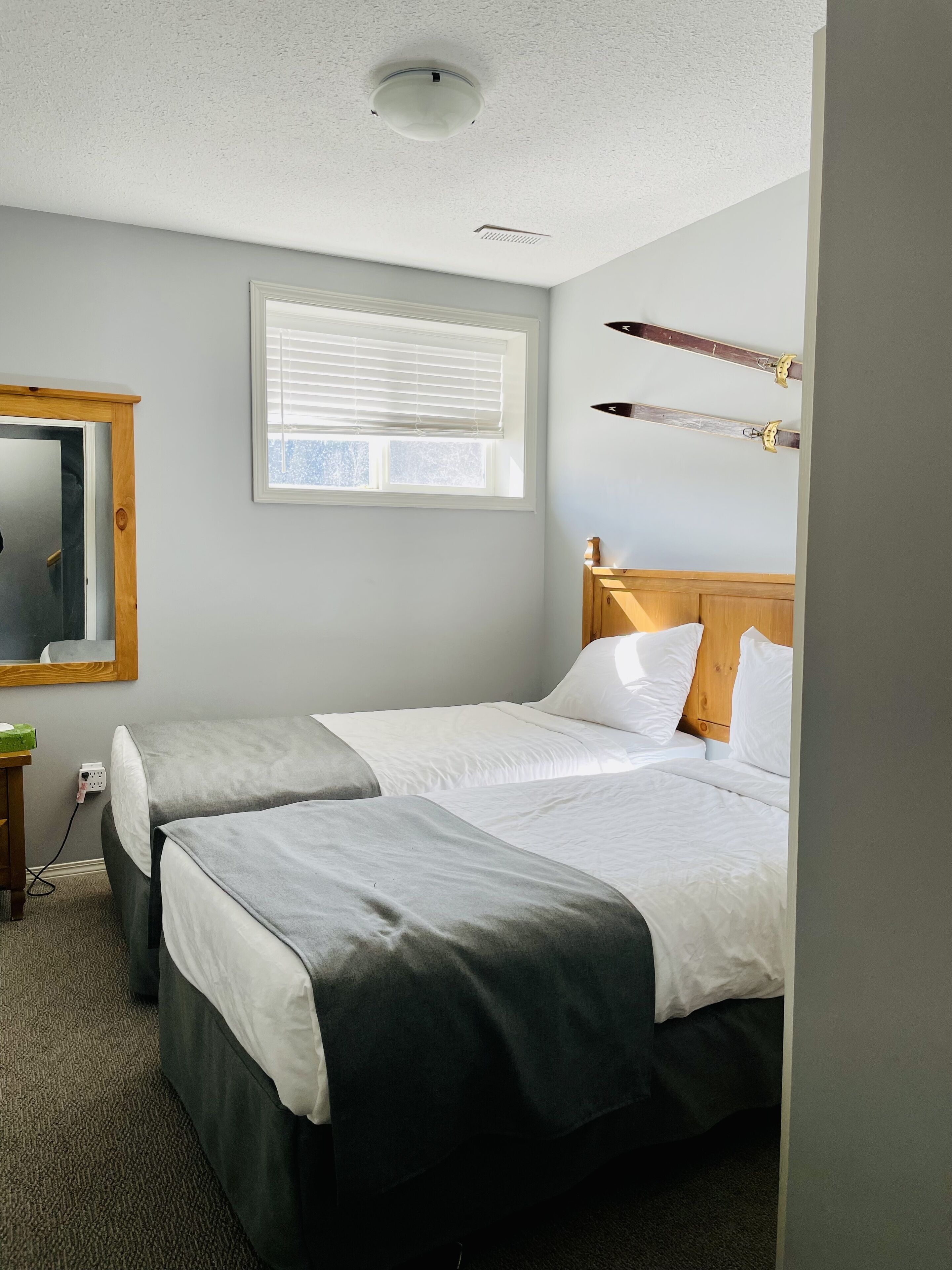 A hotel room with two beds, a window with blinds, a mirror, and a wooden headboard.