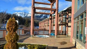 A building with a wooden deck, a snow-covered garden, and a mountain backdrop.
