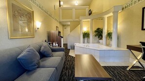 A hotel lobby with a grey sofa, a wooden coffee table, a large framed artwork, a staircase, and a spa area with a bathtub.