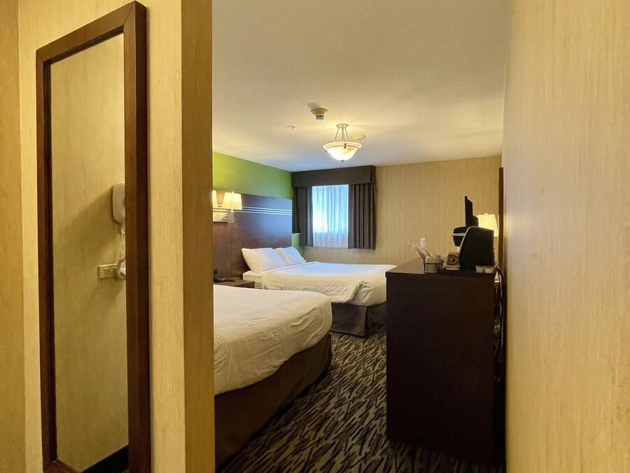 A hotel room with two beds, a desk, a mirror, and a carpeted floor.