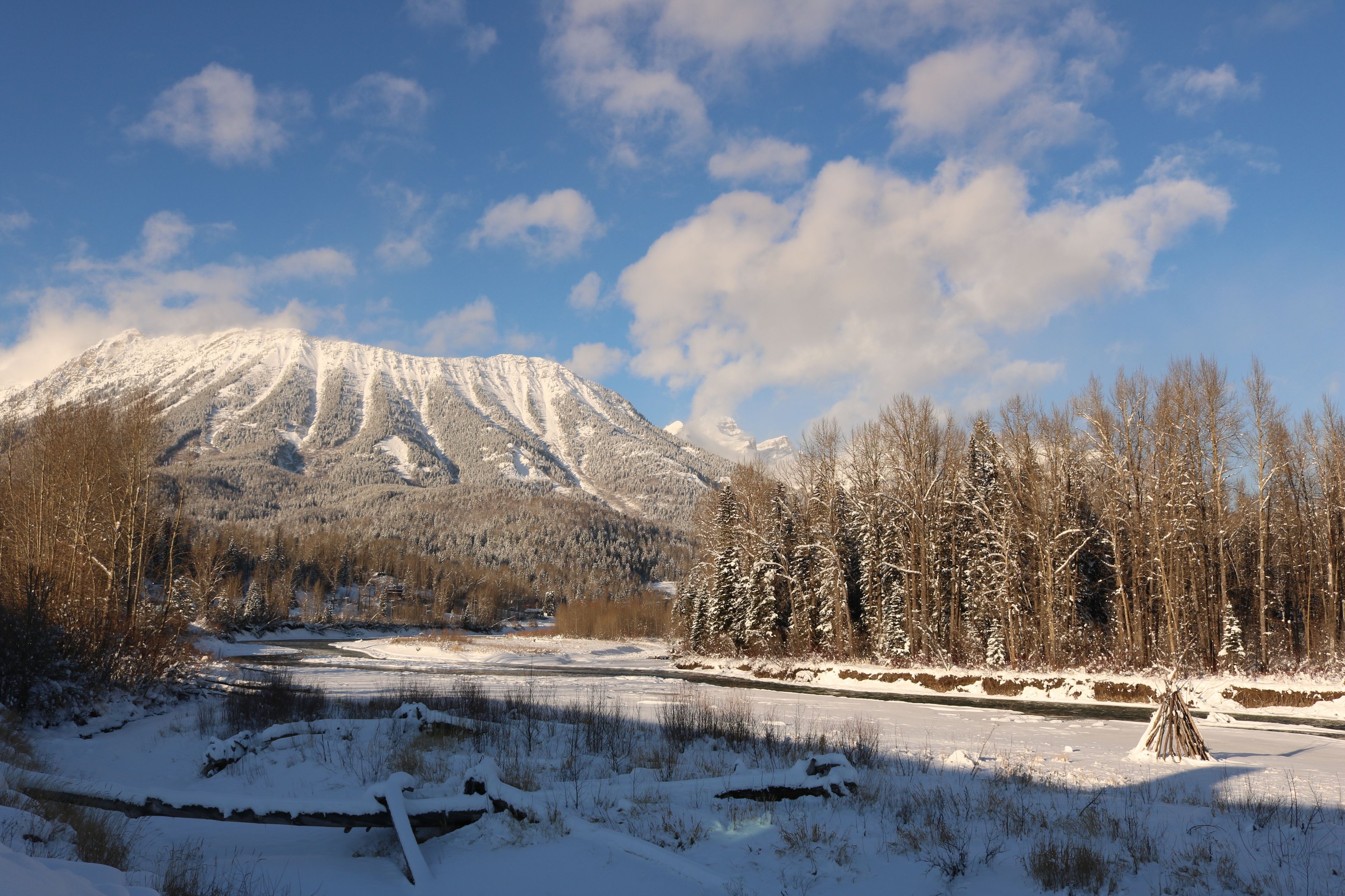 A snowy landscape with a mountain, a river, and a forest.