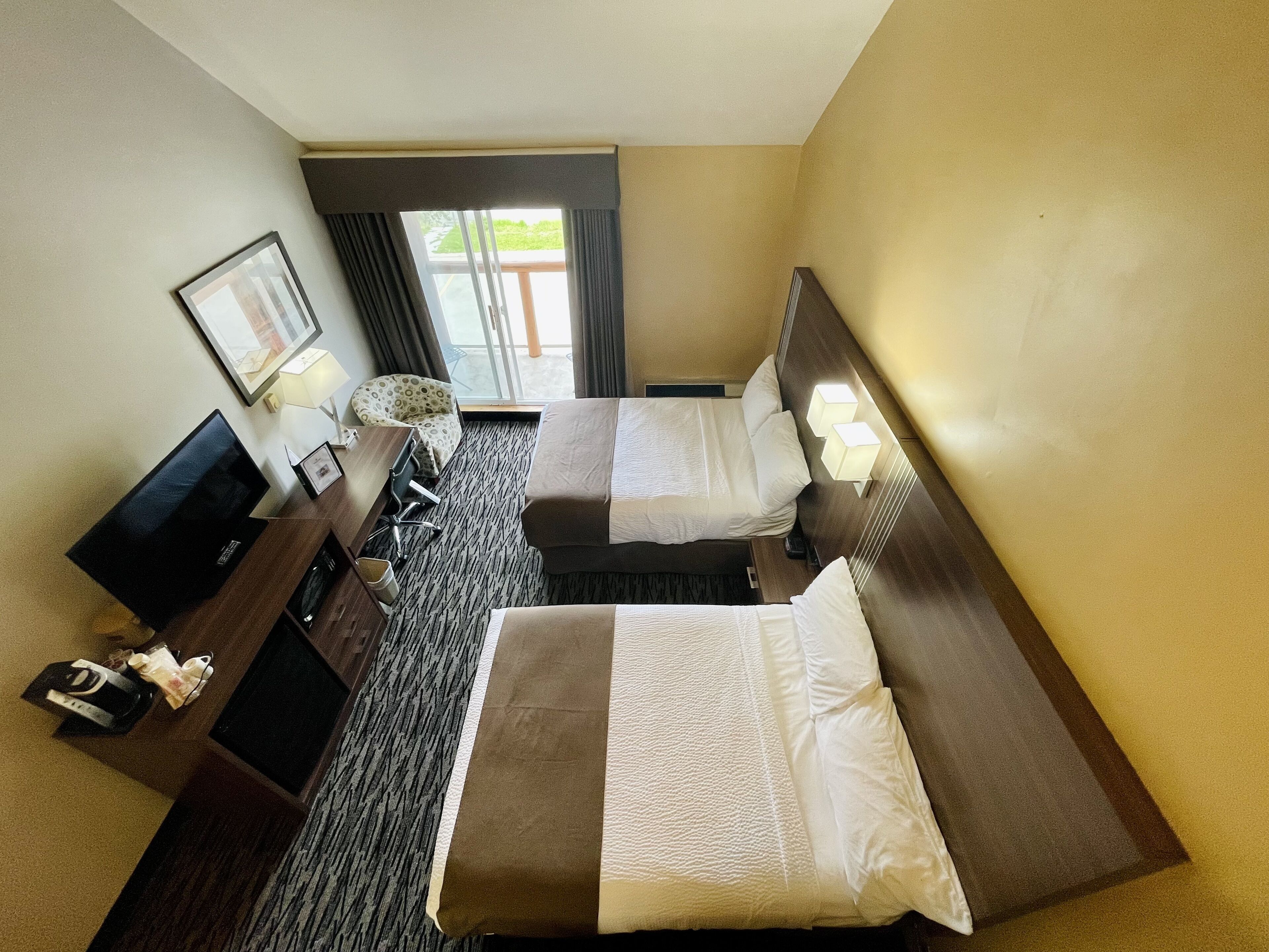 A hotel room with two beds, a desk, a TV, and a window with curtains.