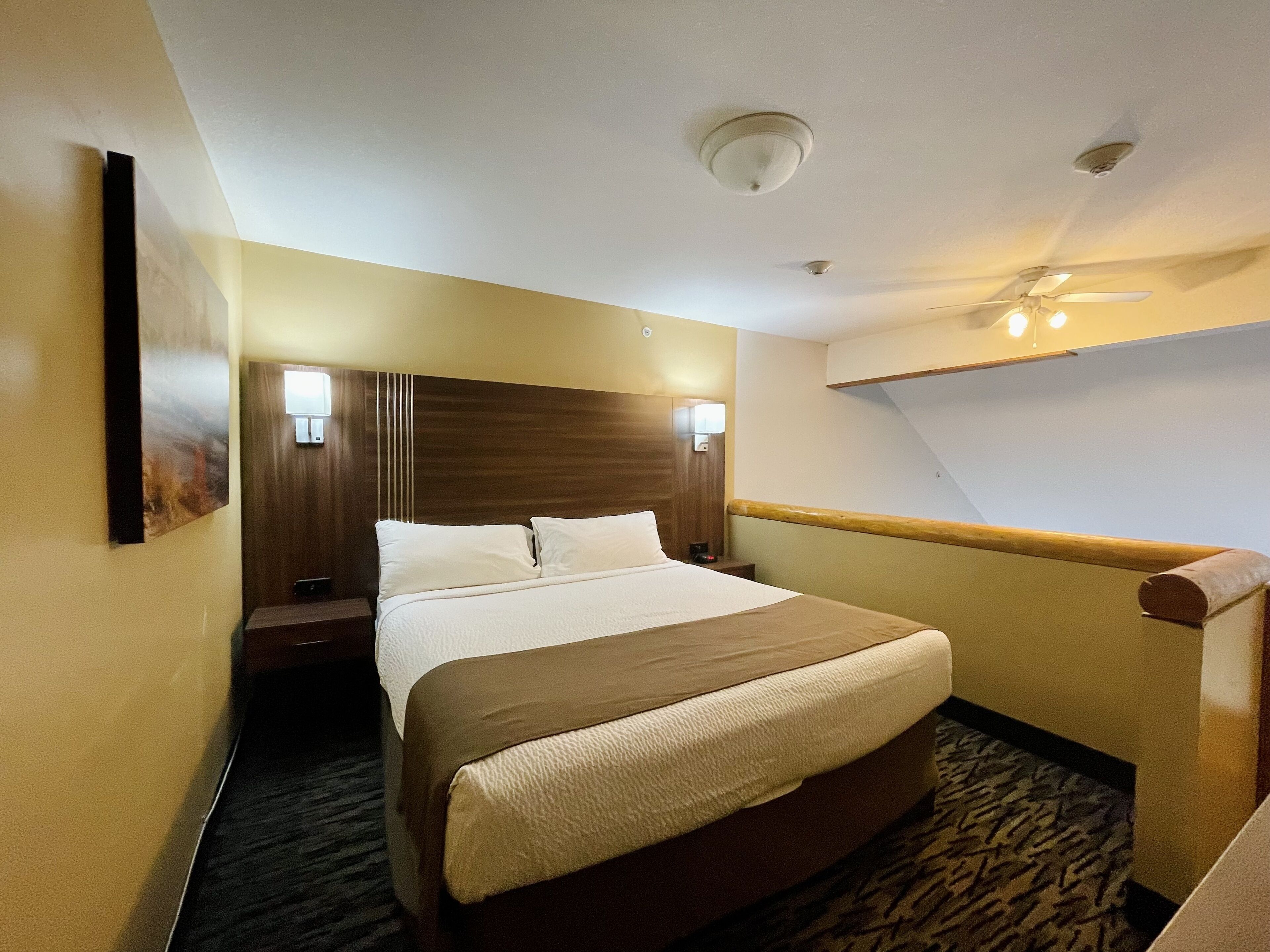 Una habitación de hotel con una cama grande, un cabecero de madera, dos lámparas de noche, un ventilador de techo y una mesita de noche con lámpara.