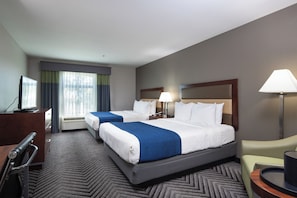 A hotel room with two beds, a desk, a chair, a TV, and a window with curtains.