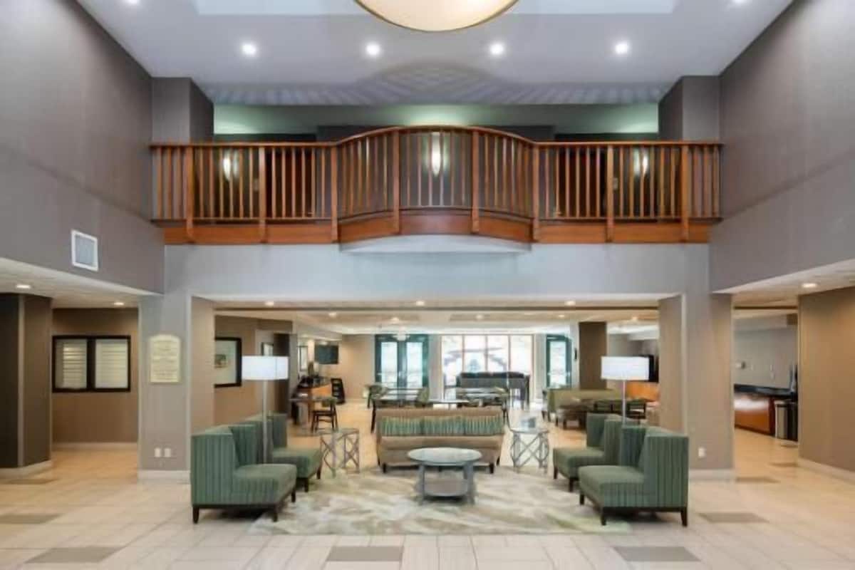 A spacious lobby with a high ceiling, a mezzanine level with a wooden railing, and a central seating area with sofas and a coffee table.