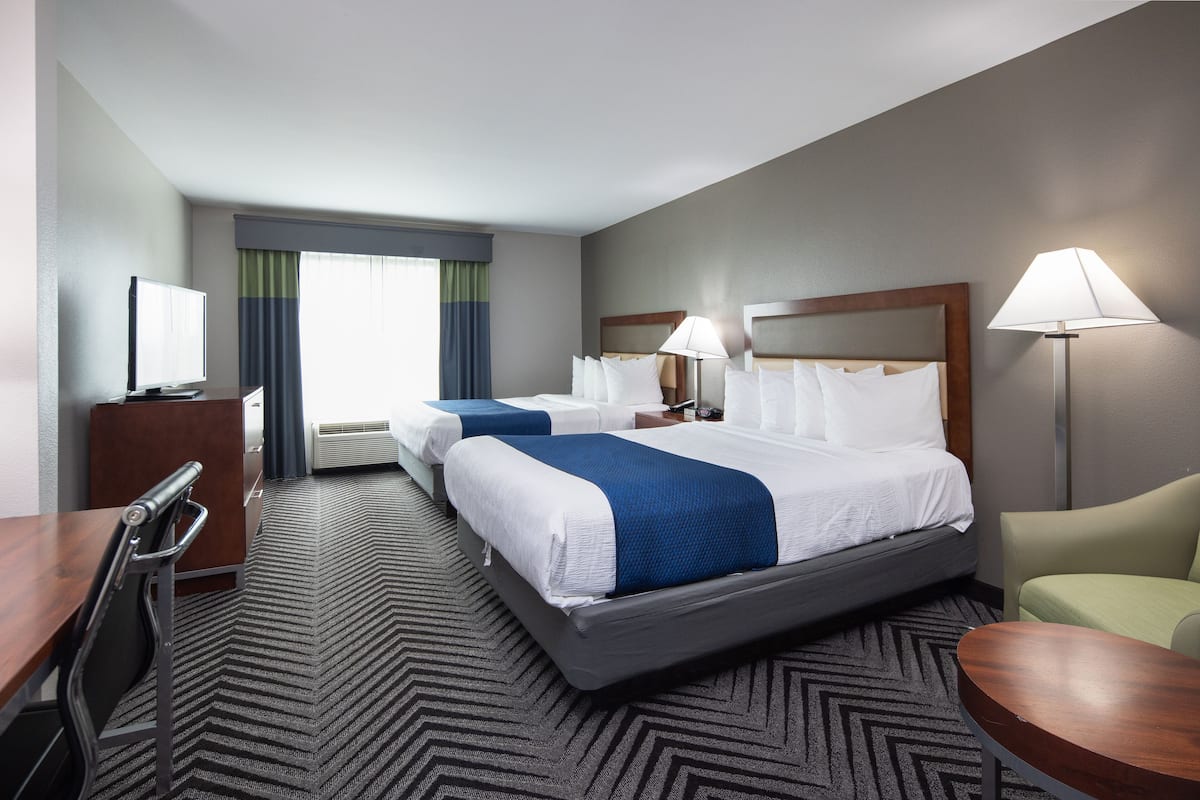 A hotel room with two beds, a desk, a chair, and a TV.