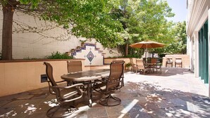 Une terrasse extérieure avec un sol carrelé, une table ronde entourée de chaises et un parasol.
