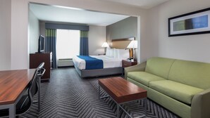 Une chambre d’hôtel avec un lit, un canapé vert, un bureau avec une chaise, une télévision et un tableau encadré au mur.