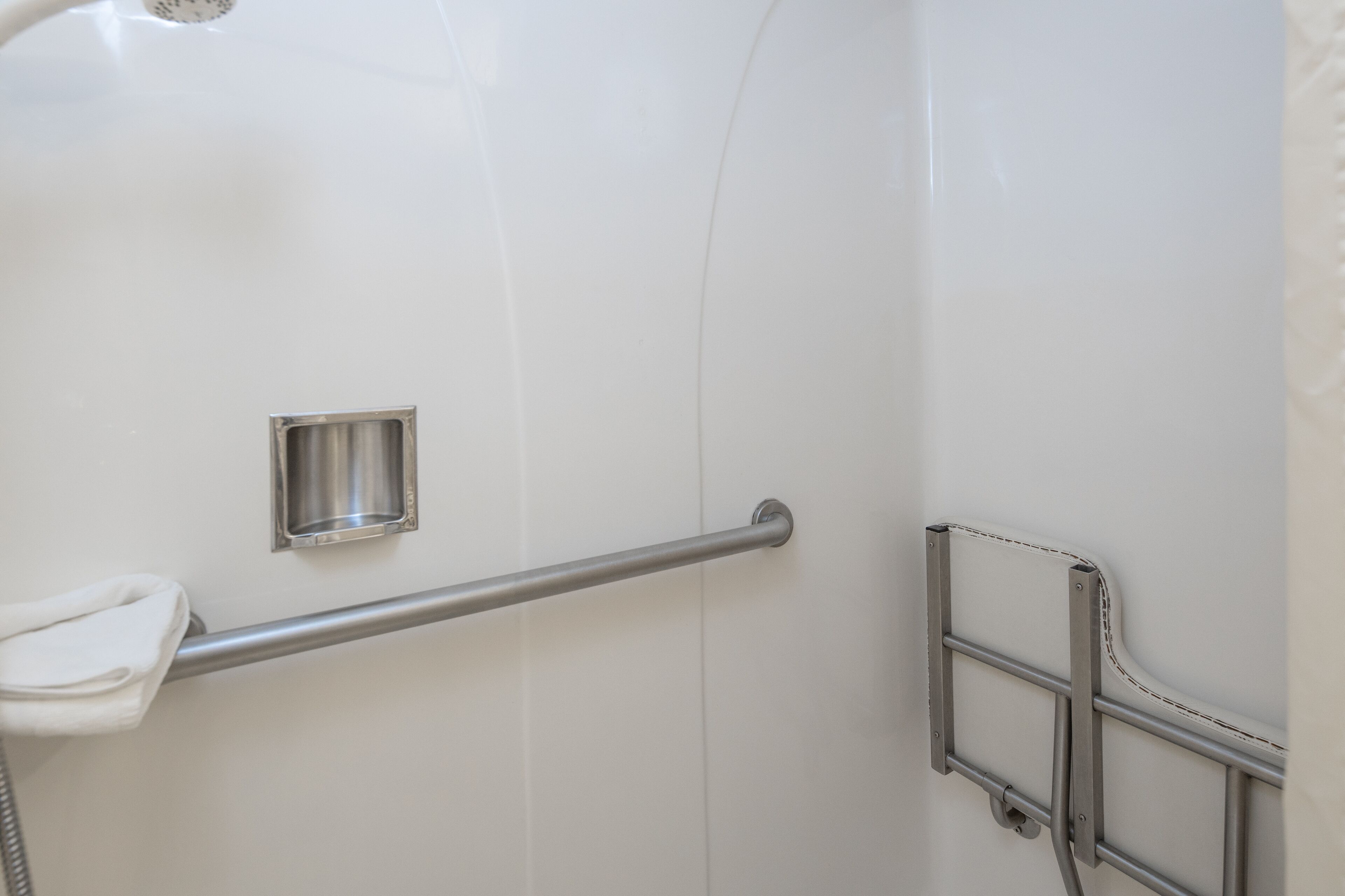 Een badkamer met een witte betegelde wand, een handgreep, een handdoekhouder en een douchepaneel.