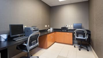 Un espacio de oficina moderno con dos escritorios, sillas, una impresora y un monitor de computadora.