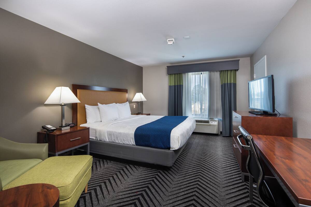 A hotel room with a bed, bedside tables, a desk, a chair, a television, and a window with curtains.
