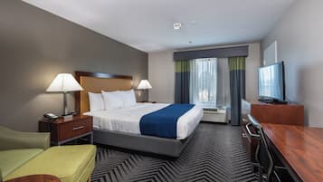 A hotel room with a bed, bedside tables, a desk, a chair, a television, and a window with curtains.