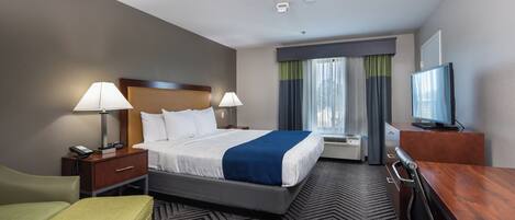 A hotel room with a bed, bedside tables, a desk, a chair, a television, and a window with curtains.