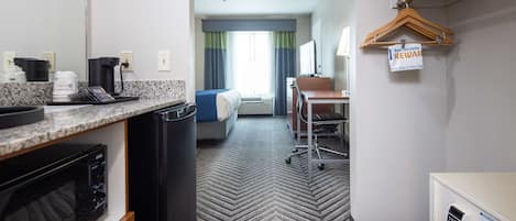 A hotel room with a kitchenette, a bed with a blue headboard, a desk with a chair, and a sign indicating a reward program.