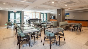 Un vaste espace dédié à la salle à manger, avec de nombreuses tables et chaises, un comptoir équipé d’un téléviseur et de grandes fenêtres laissant entrer la lumière naturelle.