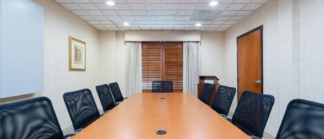 A conference room with a long wooden table, black mesh chairs, a framed picture on the wall, and a door with a wooden panel.