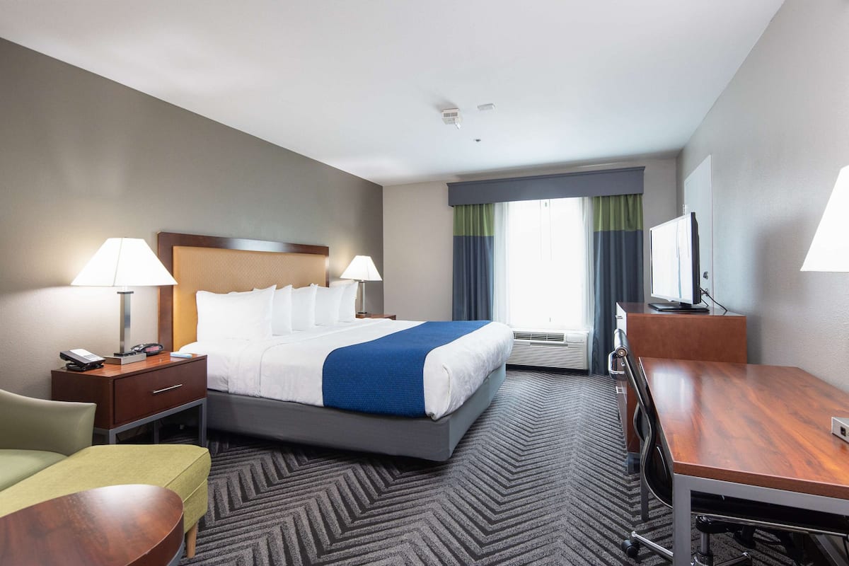 A hotel room with a bed, bedside tables, a desk, a chair, and a television.