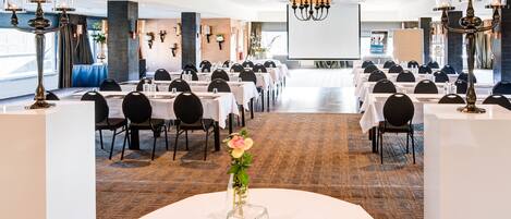 Un salón de conferencias con varias mesas y sillas, una pantalla grande y candelabros decorativos.