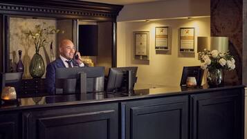 A reception desk with a man seated behind it, framed certificates on the wall, and decorative vases.