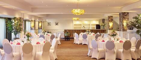 Un salón de banquetes con mesas redondas dispuestas para un evento formal, con manteles blancos y sillas.