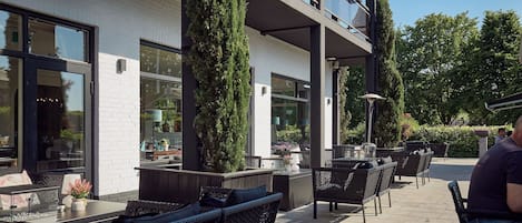 An outdoor patio area with wicker furniture, a white brick wall, and large windows.