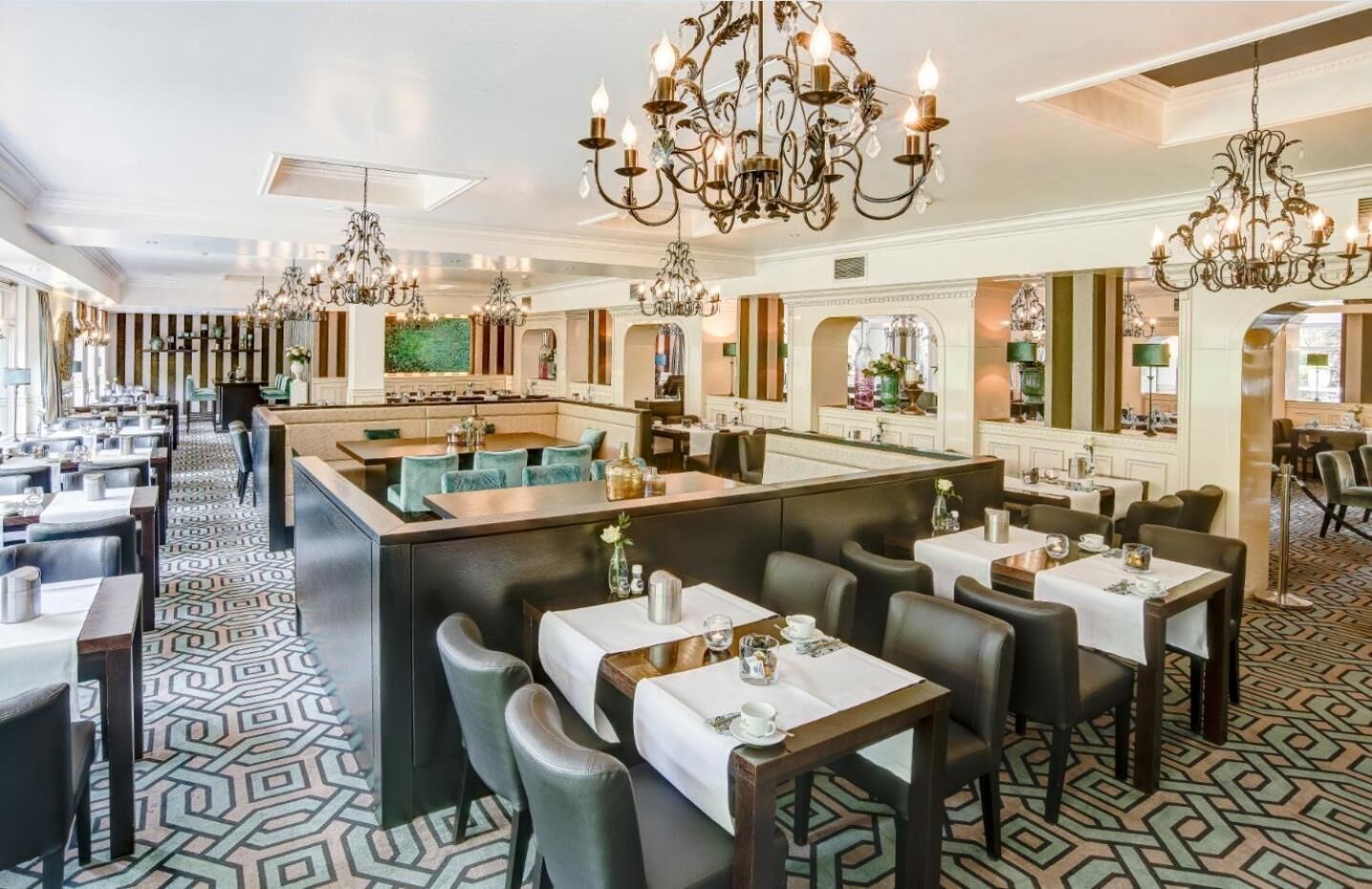 Ein geräumiges Restaurant mit hohen Decken, aufwendigen Kronleuchtern und einem gemusterten Boden.