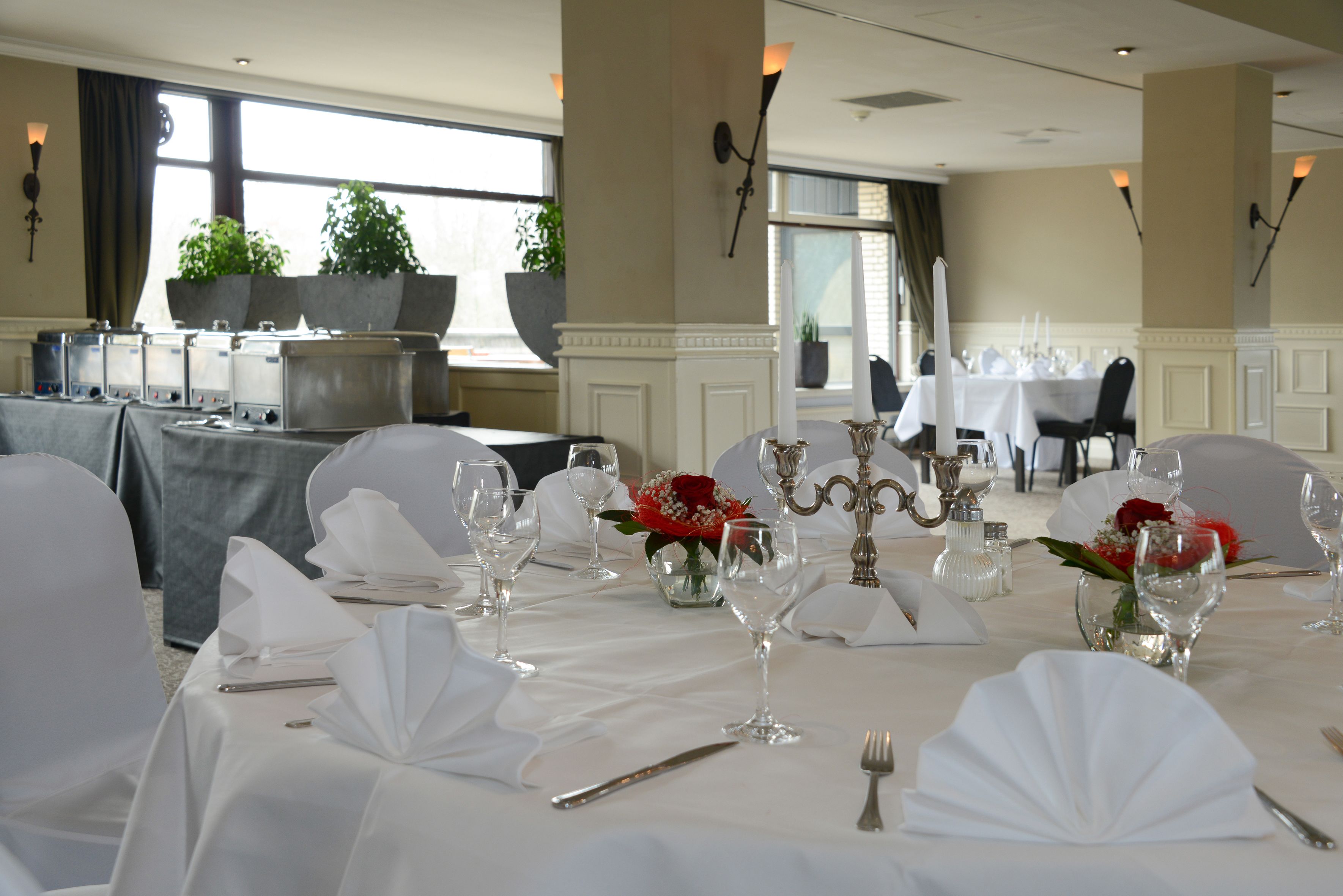 Un salón de banquetes con mesas dispuestas para un evento formal, con manteles blancos, cristalería y centros de mesa florales.