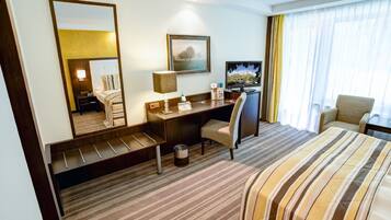 A hotel room with a bed, a desk, a chair, a television, a mirror, and a window with curtains.