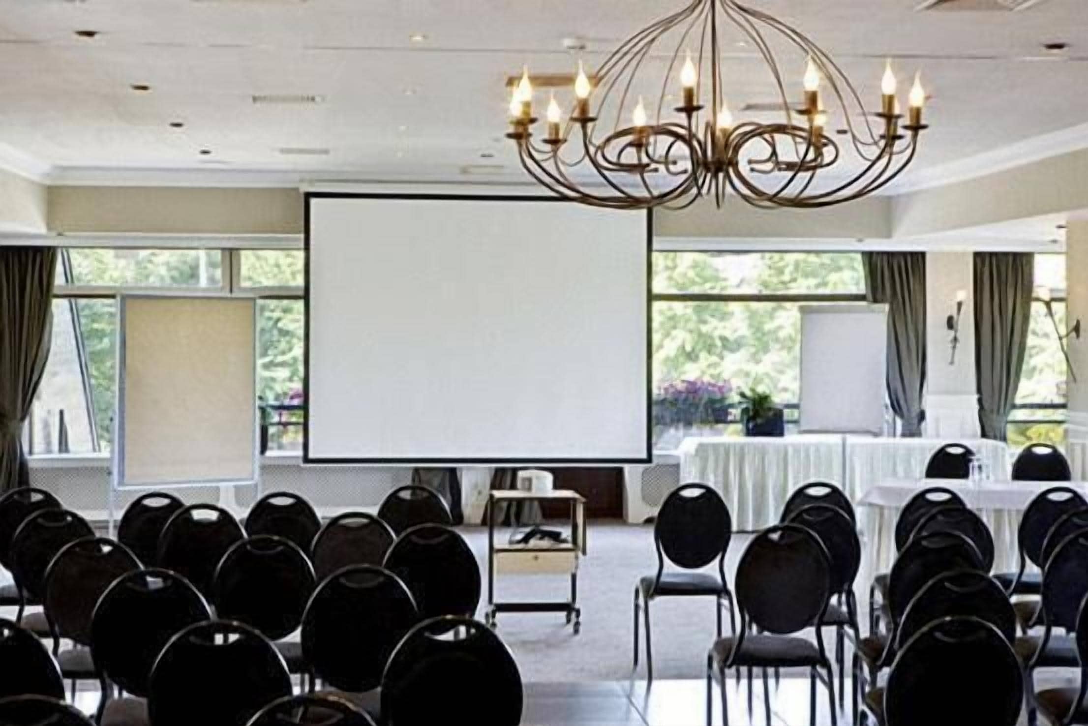 A conference room with rows of chairs, a projector screen, and a chandelier.